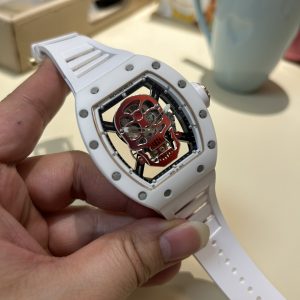 Alternative view of YS Richard Skull Ceramic Case True Tourbillon Skull Series  Richard Mille RM52-01  True Tourbillon, reinterpreting the essence of RICHARD MILLE's skull motif, overcoming bugs across multiple versions to deliver an ultra-high-quality replica with accurate dimensions, authentic movement, and meticulous detailing for dedicated collectors.Reasons to Own: 1. Near-identical dimensions: Official: 50*43*16mm; YS Factory: 49.8*44.3*16.4mm;2. Authentic Bearings: The ruby in the skull's mouth serves as the tourbillon's genuine bearing, not mere decoration. The gem aligns with the tourbillon's central axis encased by the upper and lower jaws, evoking the image of swallowing an energy sphere and capturing the sci-fi aesthetic intended by the original design.3. Meticulous Details: The inner left wall of the case cover bears the RM052 stamp identical to the original. The right eye gear matches the original in size and depth. The central gemstone on the forehead is vividly red and translucent. Features include a brushed buckle and a rubber strap made from imported Thai material.4. Movement Alignment: Thanks to the tourbillon's identical position and size to the original, the movement's operation is clearly visible from the back beneath the skull's occipital region. From the front, the black balance wheel is precisely obscured by the skull's lower jaw, leaving only the escape wheel visible beneath the skull.5. Inner and Outer Excellence: The movement is a custom-made genuine tourbillon caliber from Shanghai Watch Movement Factory. Each watch undergoes rigorous QE timing tests on a high-intensity simulator and features enhanced water resistance. JB Factory—Crafted with Heart and Soul! This is another masterpiece following the Double Tourbillon, RM001, Roger Dubuis Royal, RM053, Rolex Tourbillon, and Classic Fusion!Each YSFactory tourbillon comes with a complimentary genuine leather protective pouch.